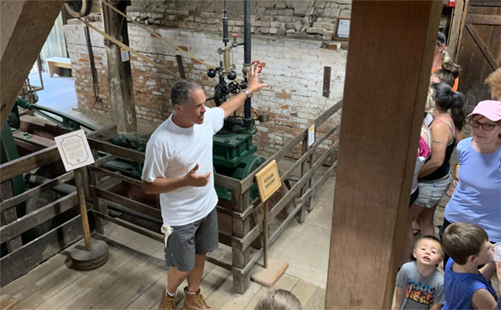 A man talking to a group of people as he gestures to machinery in the mill