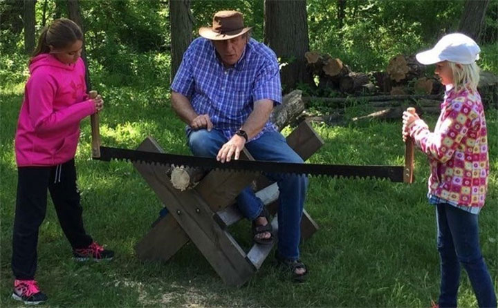 Two children using an old fashioned saw as a man supervises